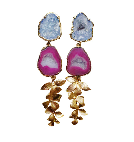 A pair of gold-tone dangle earrings featuring light blue and magenta agate geode drops with dangling gold floral leaf charms, set against a plain white background.